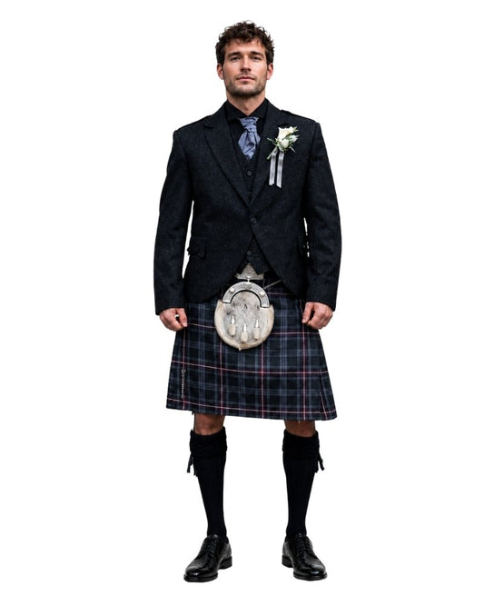 Man wearing a traditional Scottish kilt with a jacket and shoes on a white background