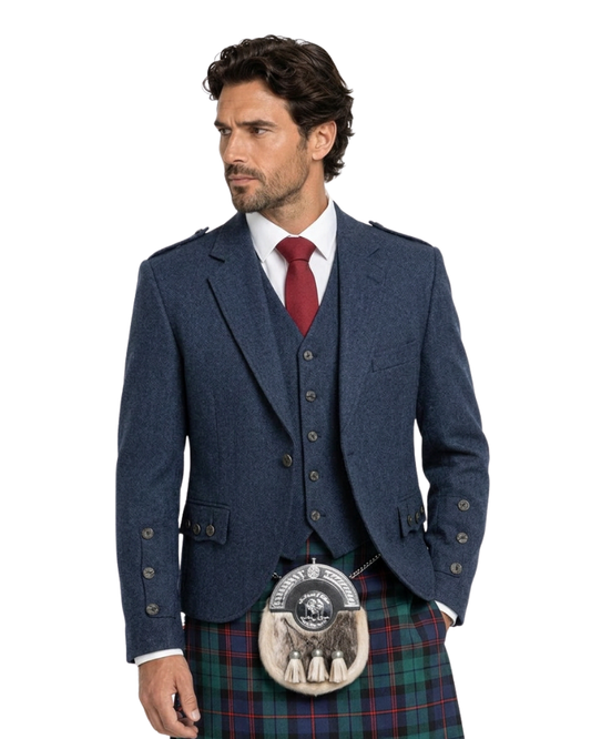 Man wearing a blue Highland jacket with a red tie and tartan kilt on a white background